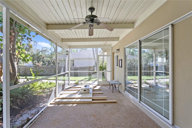 unfurnished sunroom with ceiling fan, plenty of natural light, and beamed ceiling