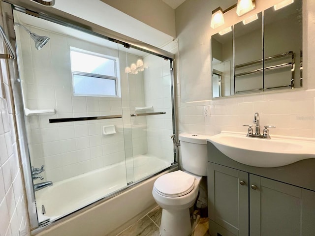 full bathroom featuring vanity, bath / shower combo with glass door, toilet, and tile walls