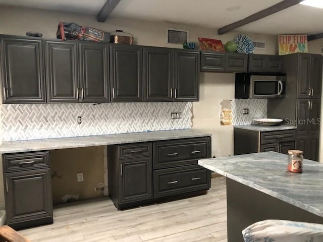 kitchen with tasteful backsplash, light stone countertops, light hardwood / wood-style floors, and beamed ceiling