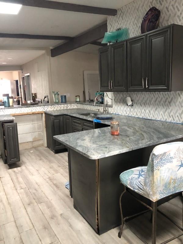 kitchen featuring sink, a breakfast bar area, light stone counters, kitchen peninsula, and beam ceiling