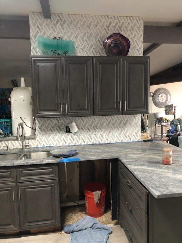 kitchen with backsplash, light stone countertops, sink, and vaulted ceiling with beams