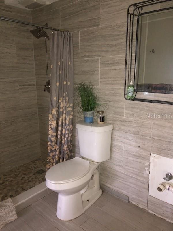 bathroom with tile walls, toilet, and a shower with shower curtain