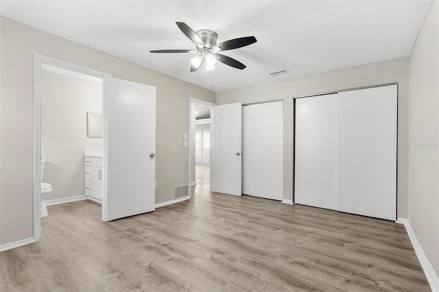 unfurnished bedroom featuring a textured ceiling, connected bathroom, light hardwood / wood-style floors, ceiling fan, and multiple closets