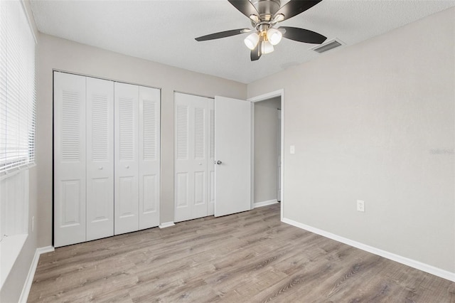 unfurnished bedroom featuring a textured ceiling, ceiling fan, light hardwood / wood-style floors, and multiple closets