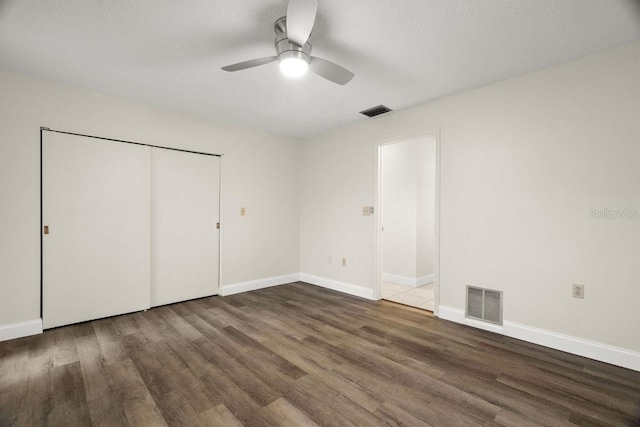 unfurnished bedroom with a closet, a textured ceiling, dark hardwood / wood-style floors, and ceiling fan