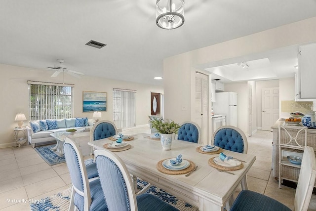 tiled dining space featuring ceiling fan and a tray ceiling