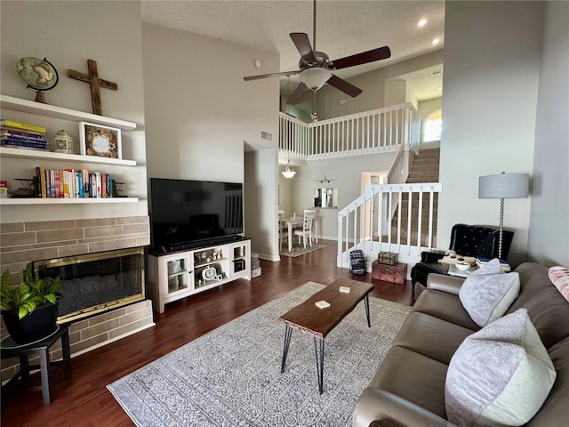 living room with a high ceiling, a textured ceiling, dark hardwood / wood-style flooring, a fireplace, and ceiling fan