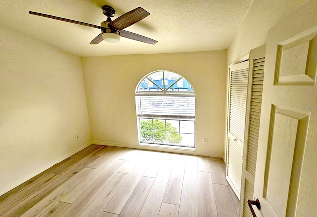 unfurnished room featuring light wood-type flooring, ceiling fan, and a textured ceiling