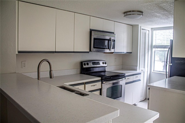 kitchen featuring kitchen peninsula, sink, appliances with stainless steel finishes, a textured ceiling, and white cabinets