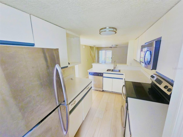 kitchen featuring appliances with stainless steel finishes, light wood-type flooring, a textured ceiling, white cabinets, and sink