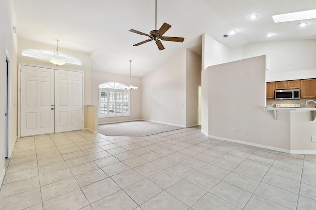 unfurnished living room featuring high vaulted ceiling, a skylight, light tile patterned flooring, and ceiling fan with notable chandelier