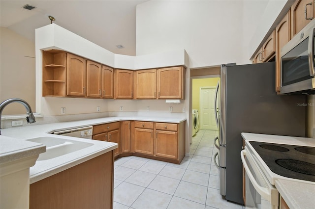 kitchen featuring independent washer and dryer, kitchen peninsula, white electric range, sink, and light tile patterned floors