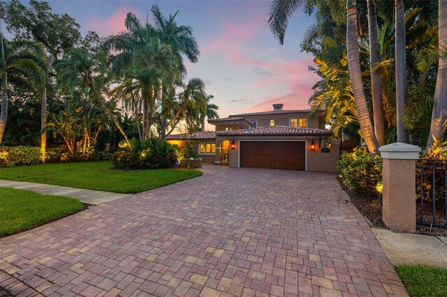 mediterranean / spanish-style home featuring a garage, a chimney, decorative driveway, a front lawn, and stucco siding