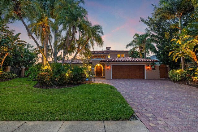 mediterranean / spanish house with a garage, a front lawn, decorative driveway, and stucco siding