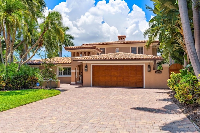 mediterranean / spanish home featuring a garage, a tile roof, decorative driveway, and stucco siding