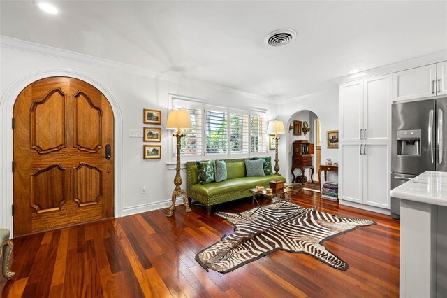 foyer entrance featuring arched walkways, dark wood-type flooring, visible vents, baseboards, and ornamental molding