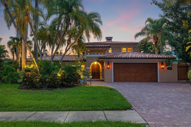 mediterranean / spanish-style house with a garage, a tile roof, decorative driveway, a lawn, and stucco siding