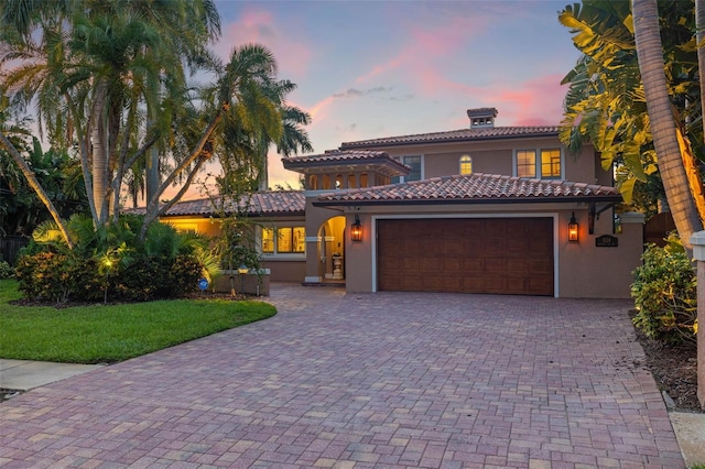 mediterranean / spanish-style house with a garage, a front yard, decorative driveway, and stucco siding