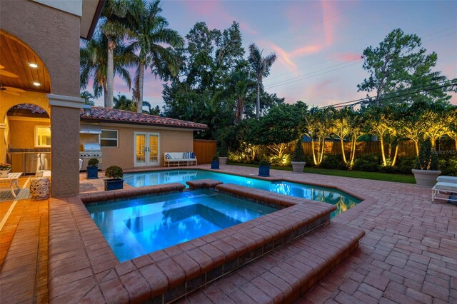 view of swimming pool with french doors, a patio, an in ground hot tub, exterior kitchen, and a fenced backyard