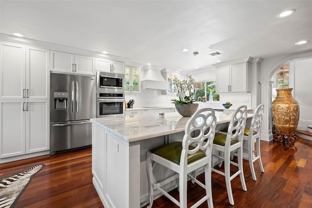 kitchen featuring light stone counters, appliances with stainless steel finishes, white cabinetry, a kitchen island, and premium range hood