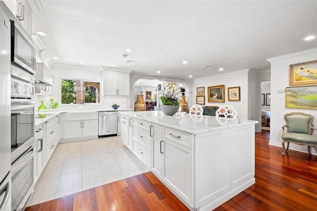 kitchen featuring arched walkways, crown molding, stainless steel appliances, white cabinetry, and a kitchen island