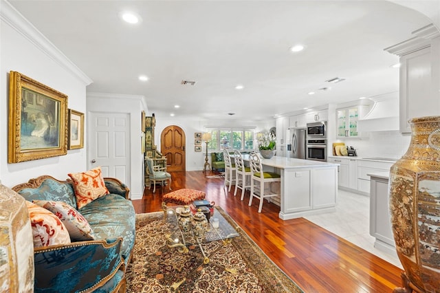 living room featuring arched walkways, recessed lighting, visible vents, light wood finished floors, and crown molding