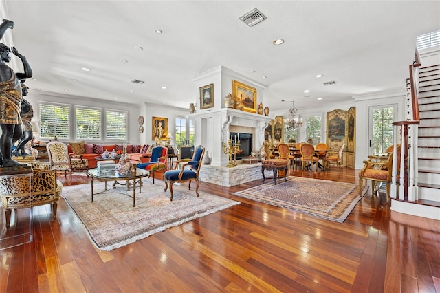 living room featuring stairs, visible vents, a fireplace with raised hearth, and wood finished floors