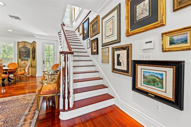 staircase featuring baseboards, visible vents, wood finished floors, and ornamental molding