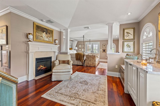 interior space with a fireplace with flush hearth, baseboards, ornamental molding, dark wood finished floors, and decorative columns