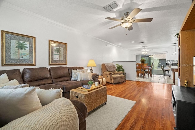 living room featuring ceiling fan, a textured ceiling, crown molding, and light wood-type flooring