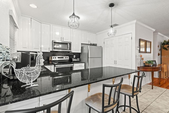 kitchen with light tile patterned floors, white cabinetry, appliances with stainless steel finishes, decorative light fixtures, and dark stone countertops