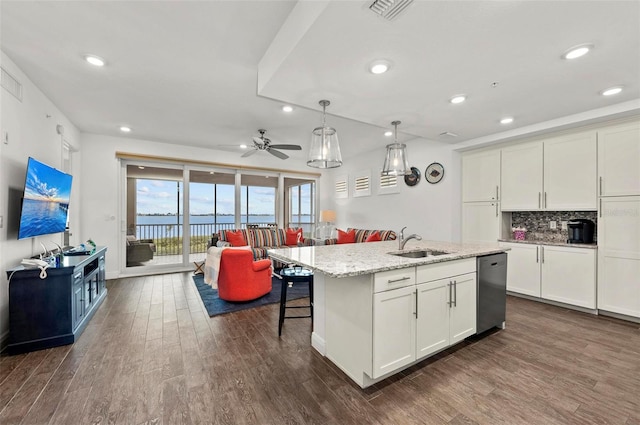 kitchen featuring light stone countertops, dishwasher, sink, hanging light fixtures, and a kitchen island with sink