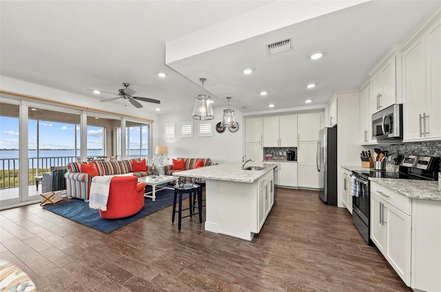 kitchen with white cabinetry, stainless steel appliances, an island with sink, backsplash, and a water view