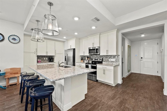 kitchen featuring light stone countertops, stainless steel appliances, white cabinets, and a kitchen island with sink