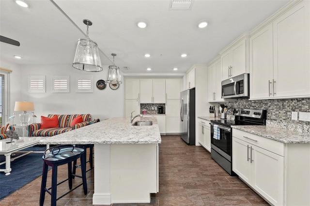 kitchen featuring tasteful backsplash, a center island with sink, white cabinetry, hanging light fixtures, and stainless steel appliances