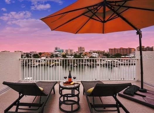 patio terrace at dusk featuring a water view and a balcony