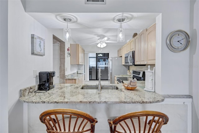 kitchen featuring sink, appliances with stainless steel finishes, hanging light fixtures, light stone counters, and kitchen peninsula