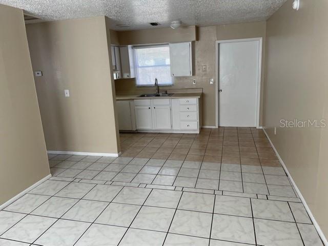 kitchen featuring white cabinets, sink, light tile patterned floors, and a textured ceiling