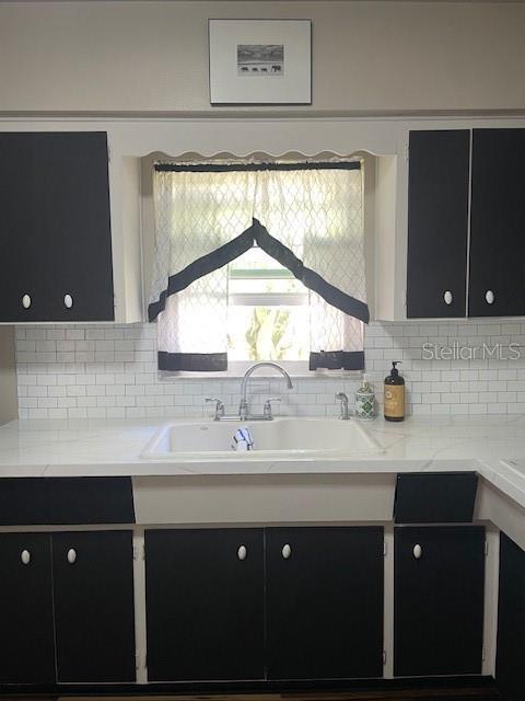 kitchen featuring light stone countertops, a sink, dark cabinetry, and decorative backsplash