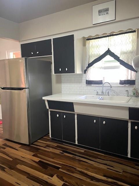 kitchen featuring a sink, light countertops, freestanding refrigerator, dark cabinetry, and dark wood-style floors