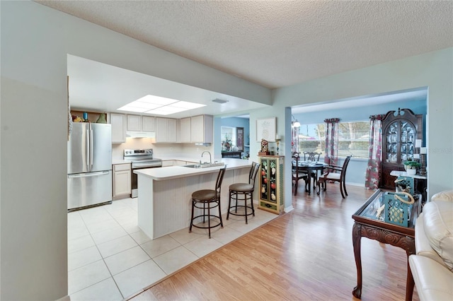 kitchen featuring a breakfast bar area, appliances with stainless steel finishes, white cabinets, a textured ceiling, and light hardwood / wood-style flooring