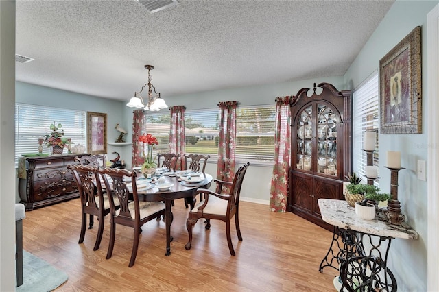 dining area featuring light wood-type flooring, an inviting chandelier, and a textured ceiling