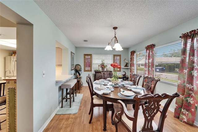 dining room with light wood-type flooring, a notable chandelier, sink, and a textured ceiling