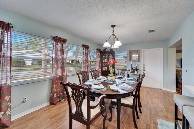 dining space with a textured ceiling, a chandelier, and light hardwood / wood-style floors