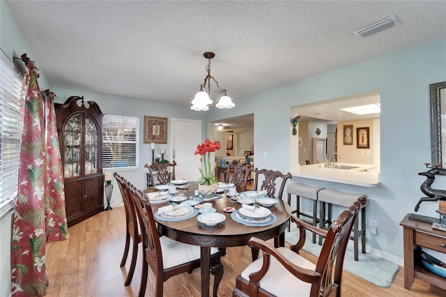 dining area with a chandelier, sink, a textured ceiling, and light hardwood / wood-style flooring