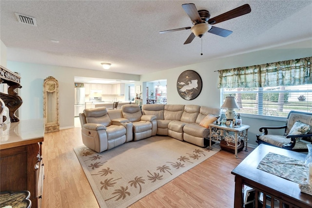 living room with light hardwood / wood-style floors, a textured ceiling, and ceiling fan