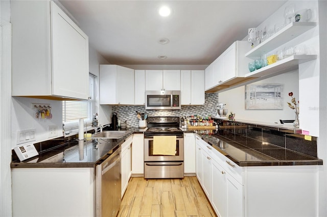 kitchen with appliances with stainless steel finishes, sink, backsplash, white cabinets, and light wood-type flooring