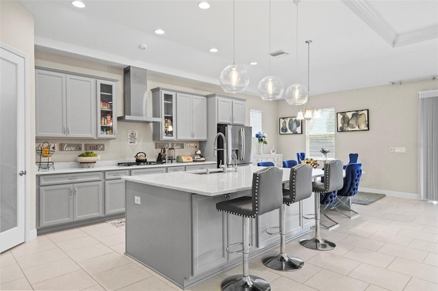 kitchen with wall chimney exhaust hood, sink, decorative light fixtures, stainless steel appliances, and a kitchen island with sink