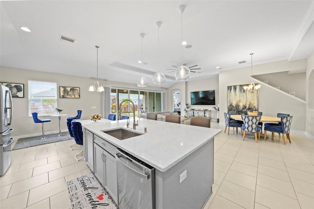 kitchen with sink, hanging light fixtures, a raised ceiling, an island with sink, and stainless steel appliances