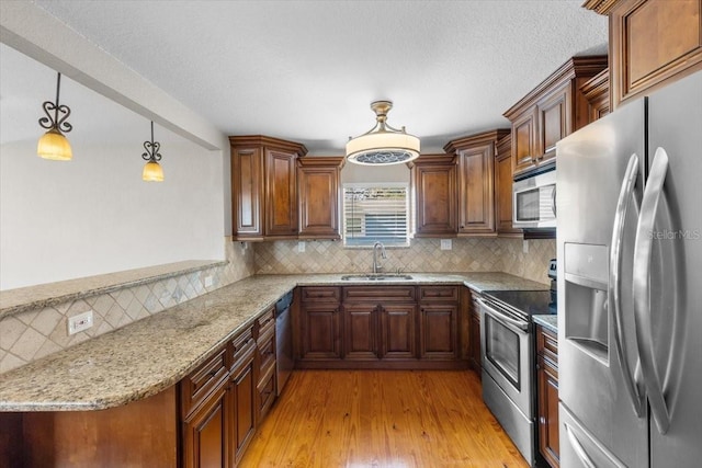 kitchen with decorative light fixtures, stainless steel appliances, sink, backsplash, and light stone counters